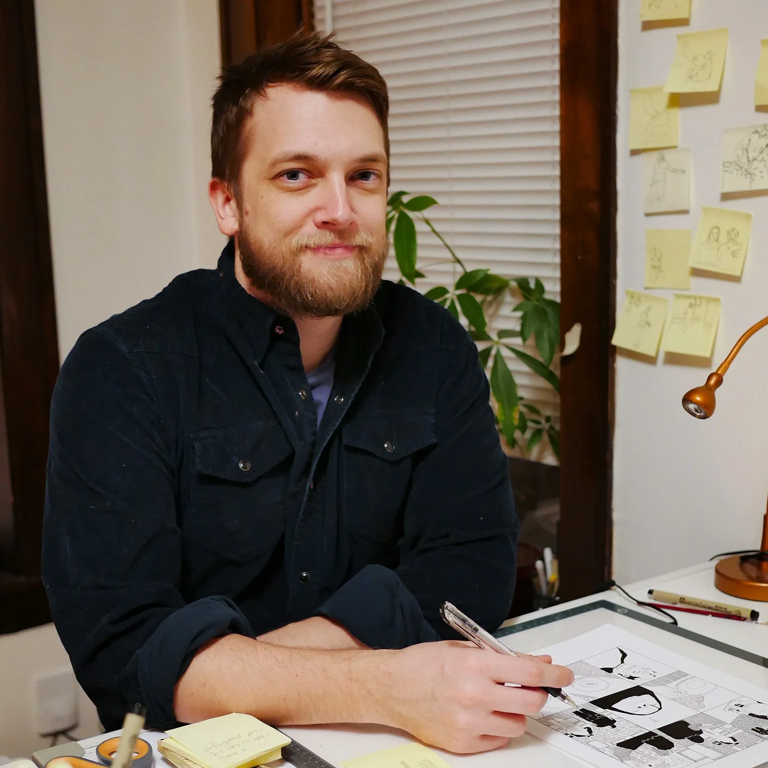 A photo of author and comic book artist T. Sean Steele at his desk, working on a black and white comic.